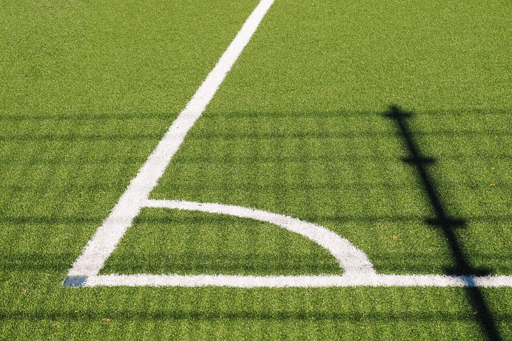 White corner markings on a sunlit artificial turf soccer pitch